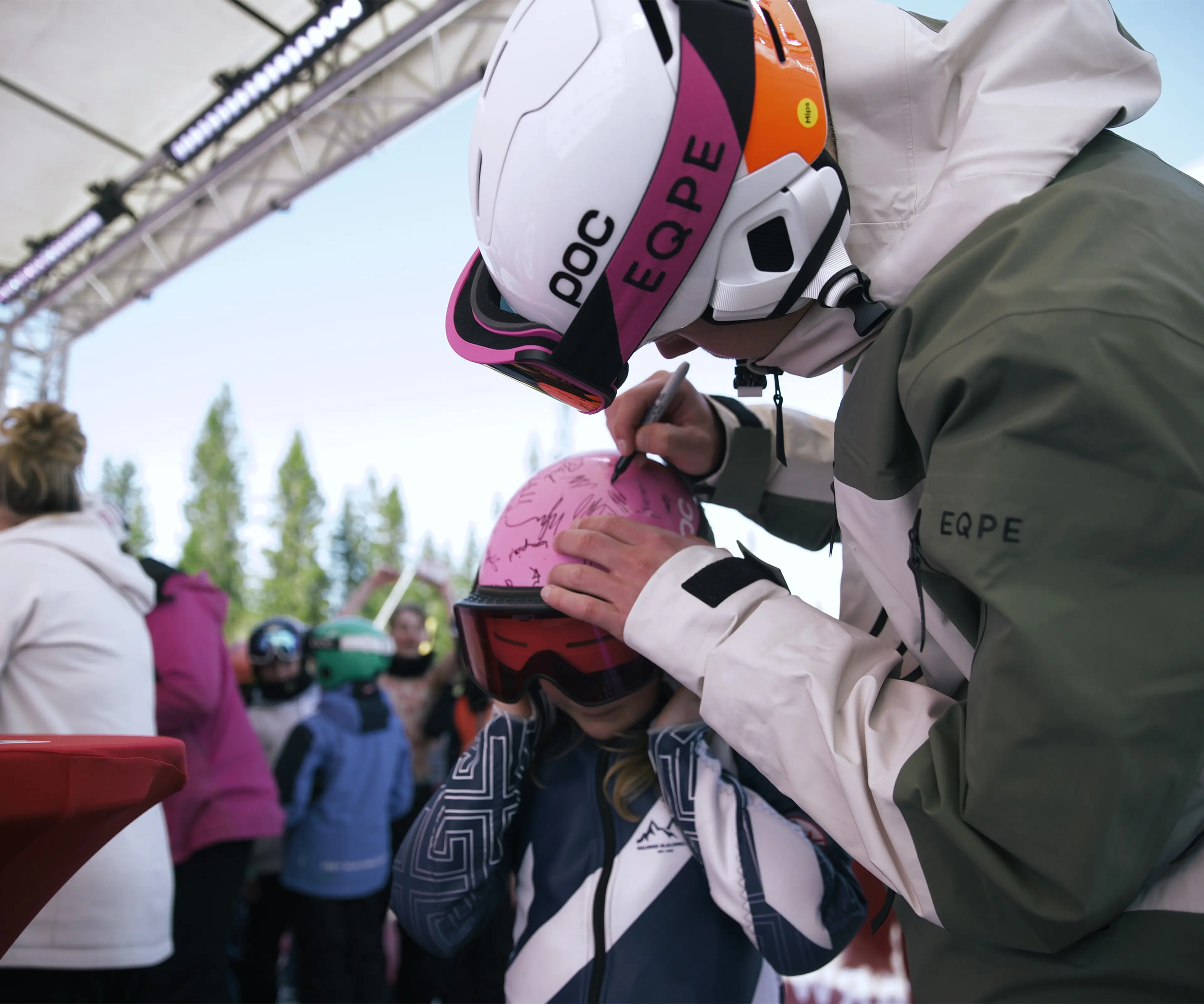 Walter Wallberg signing a child's pink helmet at SkiStar Winter Games, sorrounded by people
