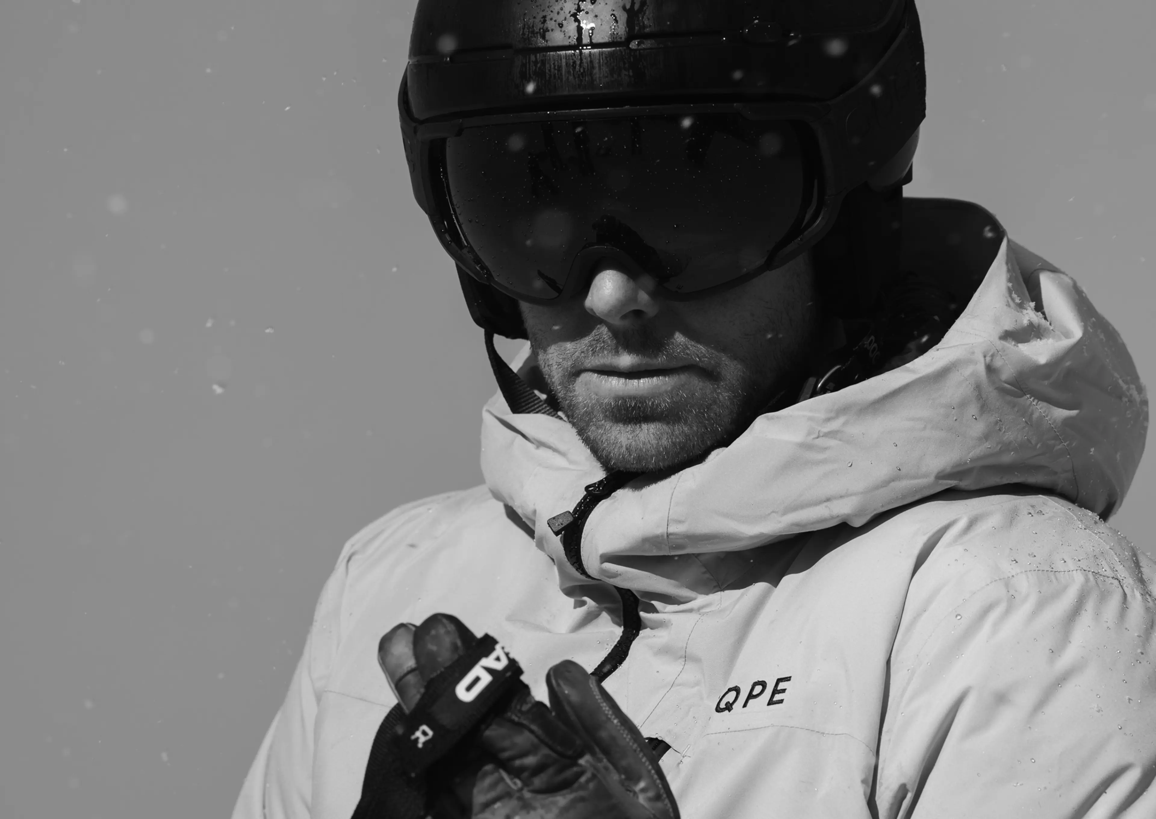 Black and white image of a person in ski gear, wearing a helmet and goggles, with snowflakes falling.