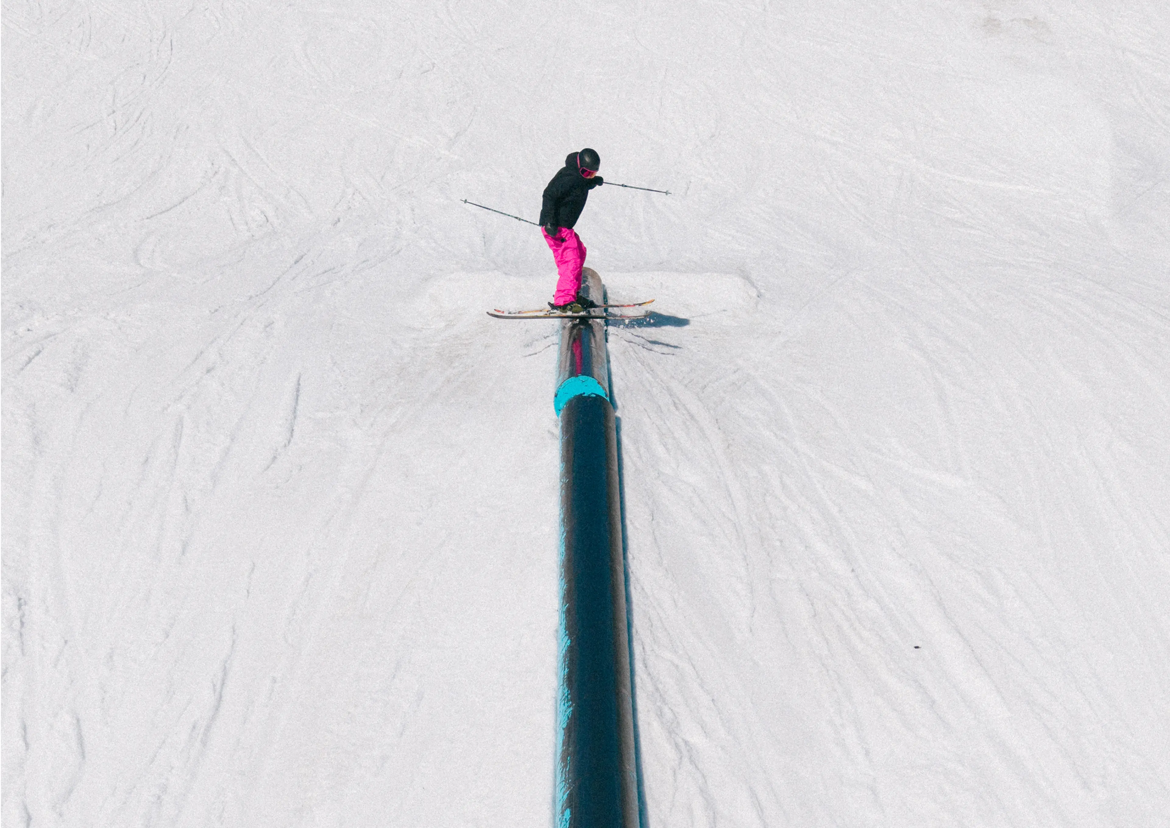 Person in pink pants skiing on a rail in a snowy terrain park.