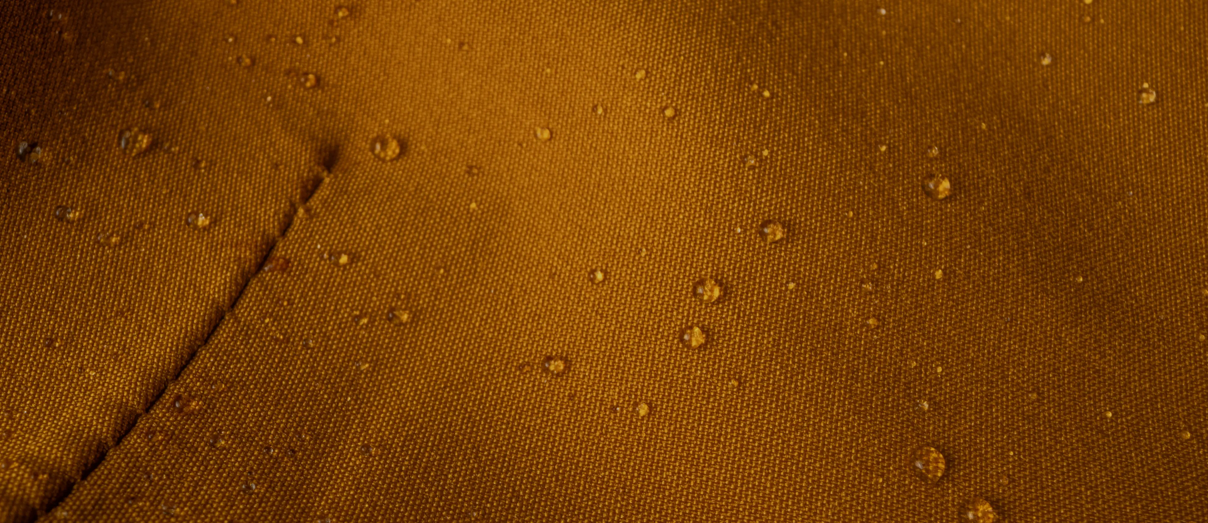 Close-up of a textured brown fabric with scattered water droplets, highlighting its water-repellent properties.