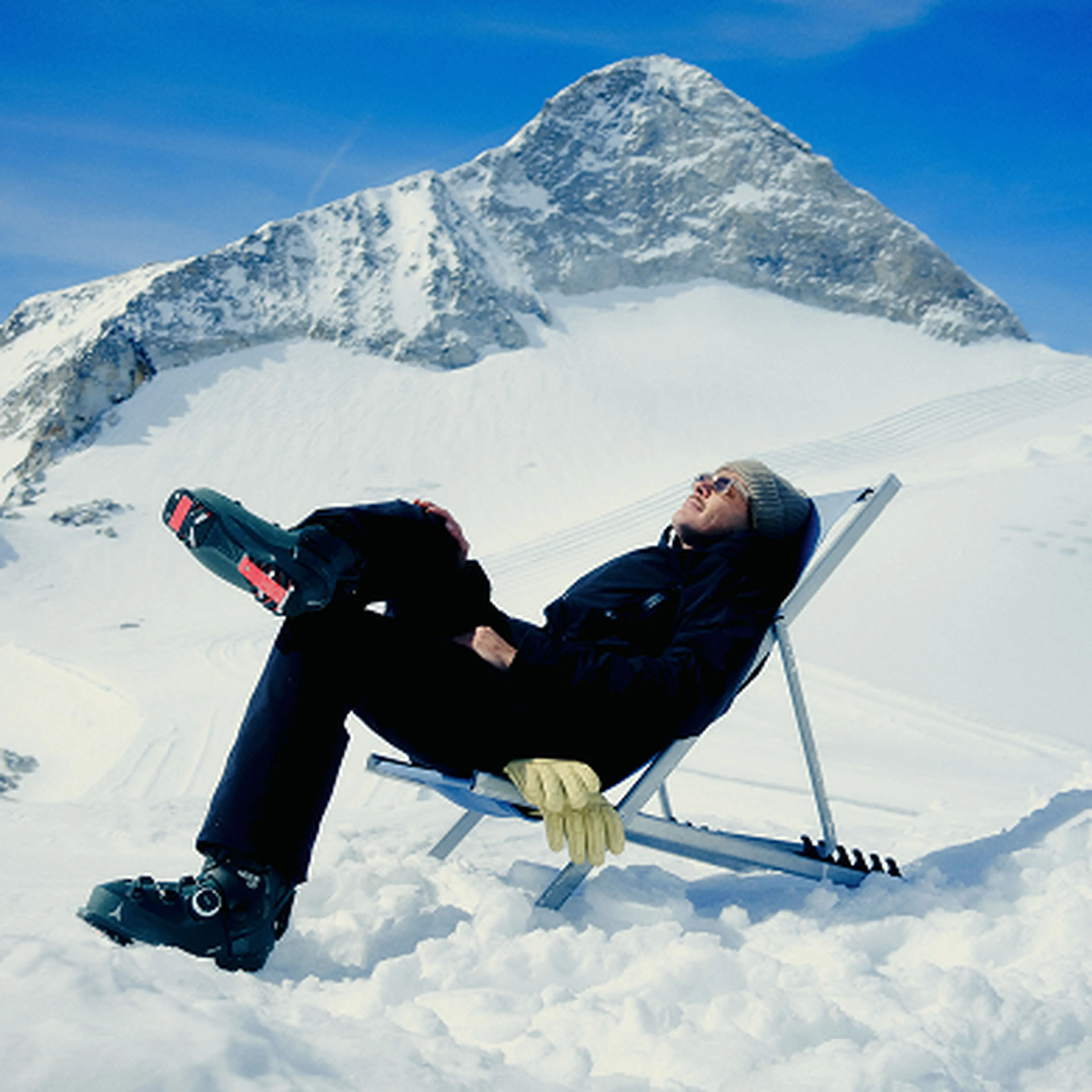 Person sitting in the sun surrounded with snowy mountains