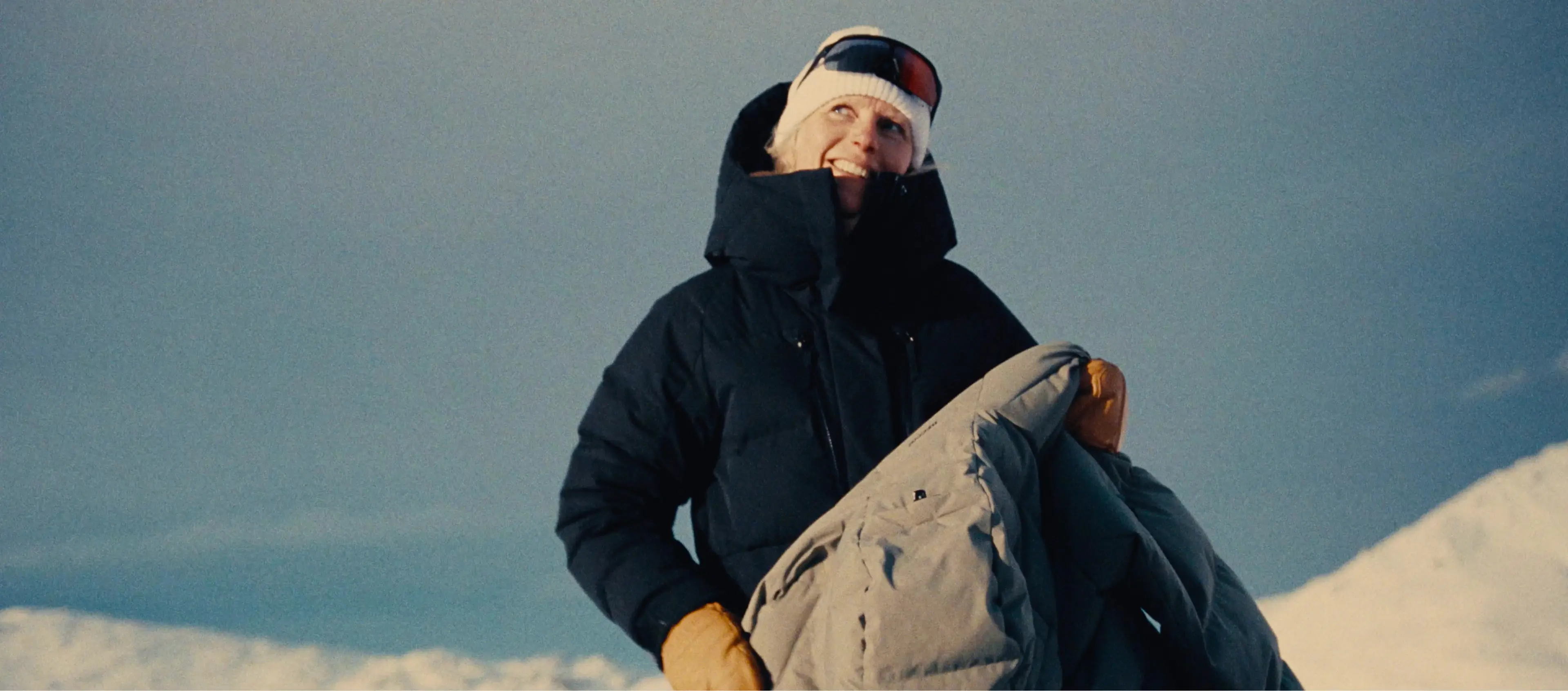 Sara smiling, wearing a winter outfit from EQPE with a snowy mountain backdrop