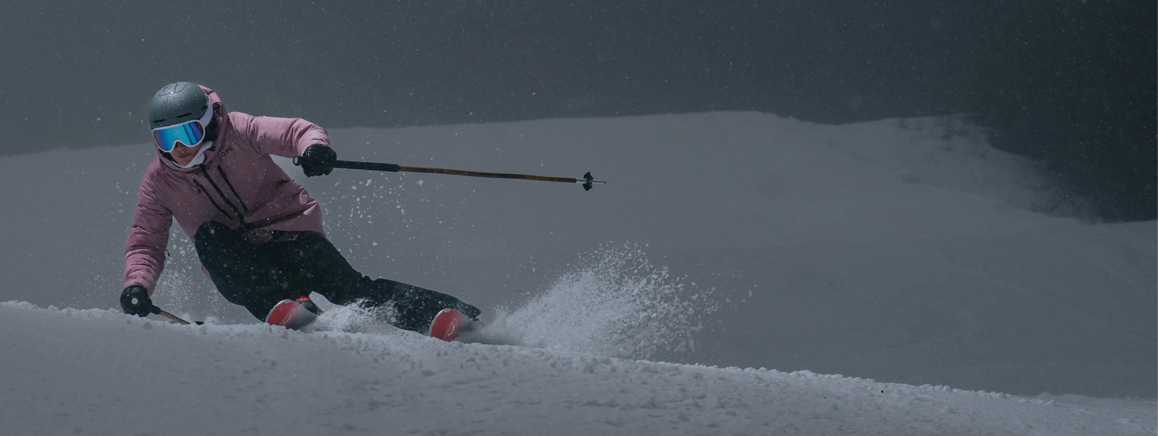 A skier in a pink jacket and helmet carving through powder snow on a misty slope.