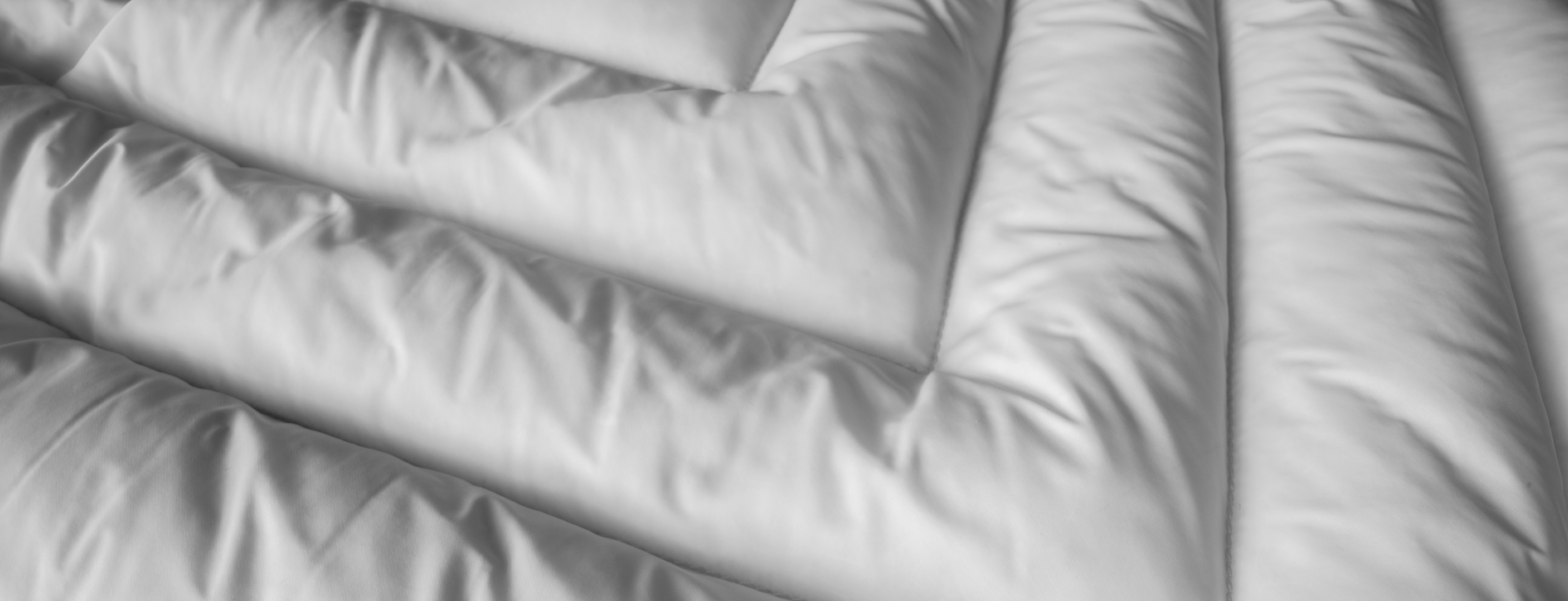 Close up picture of a white insulated lightweight jacket with down filling with seams in a fishbone pattern