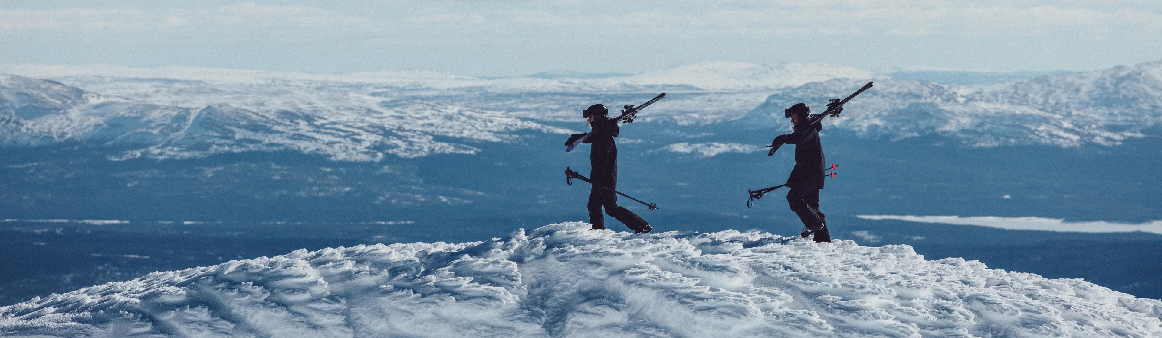 Two skiers walking on a mountain carrying ski gear