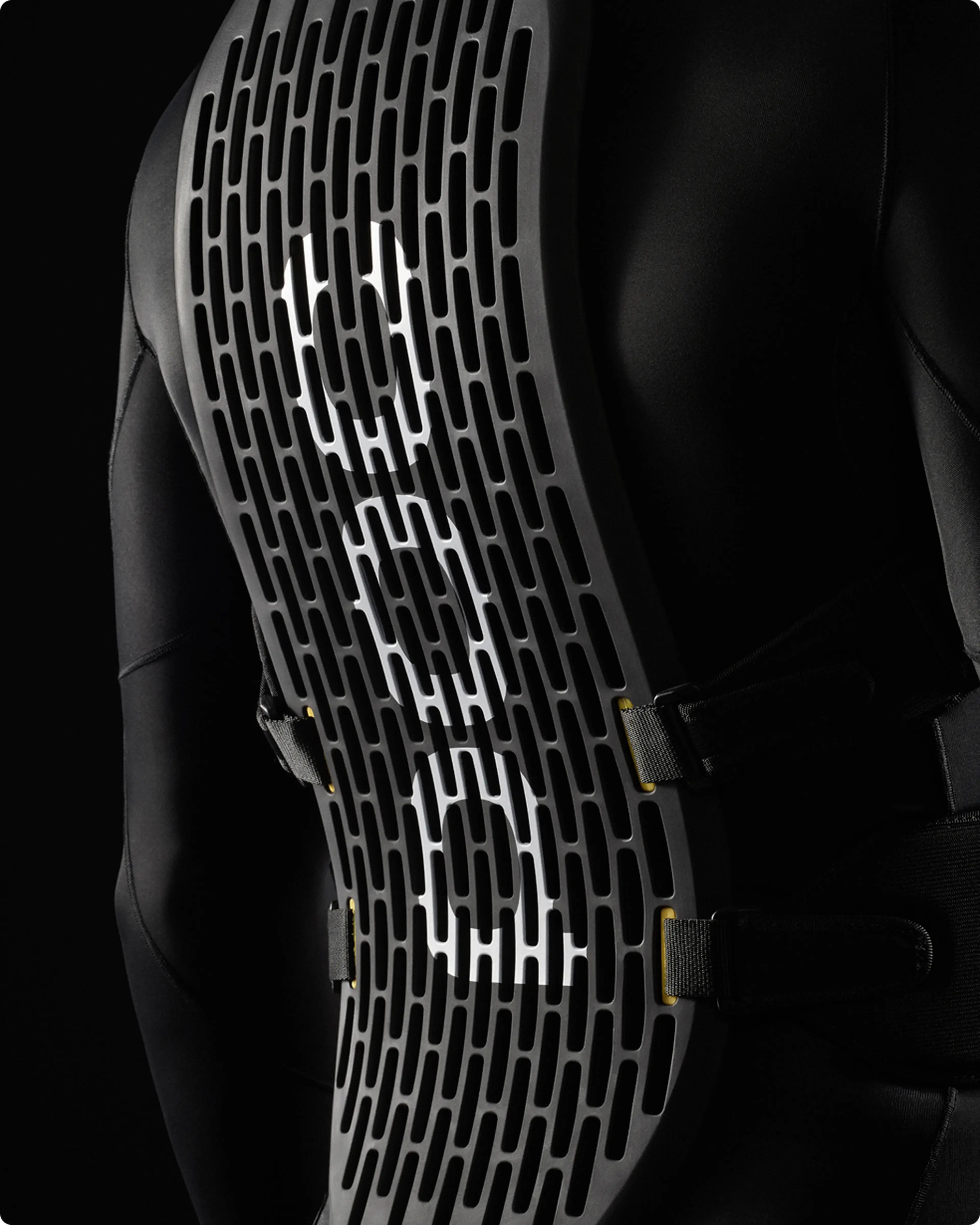 Back view of a person wearing a black protective spine guard with a grid pattern and white accents, set against a dark background.
