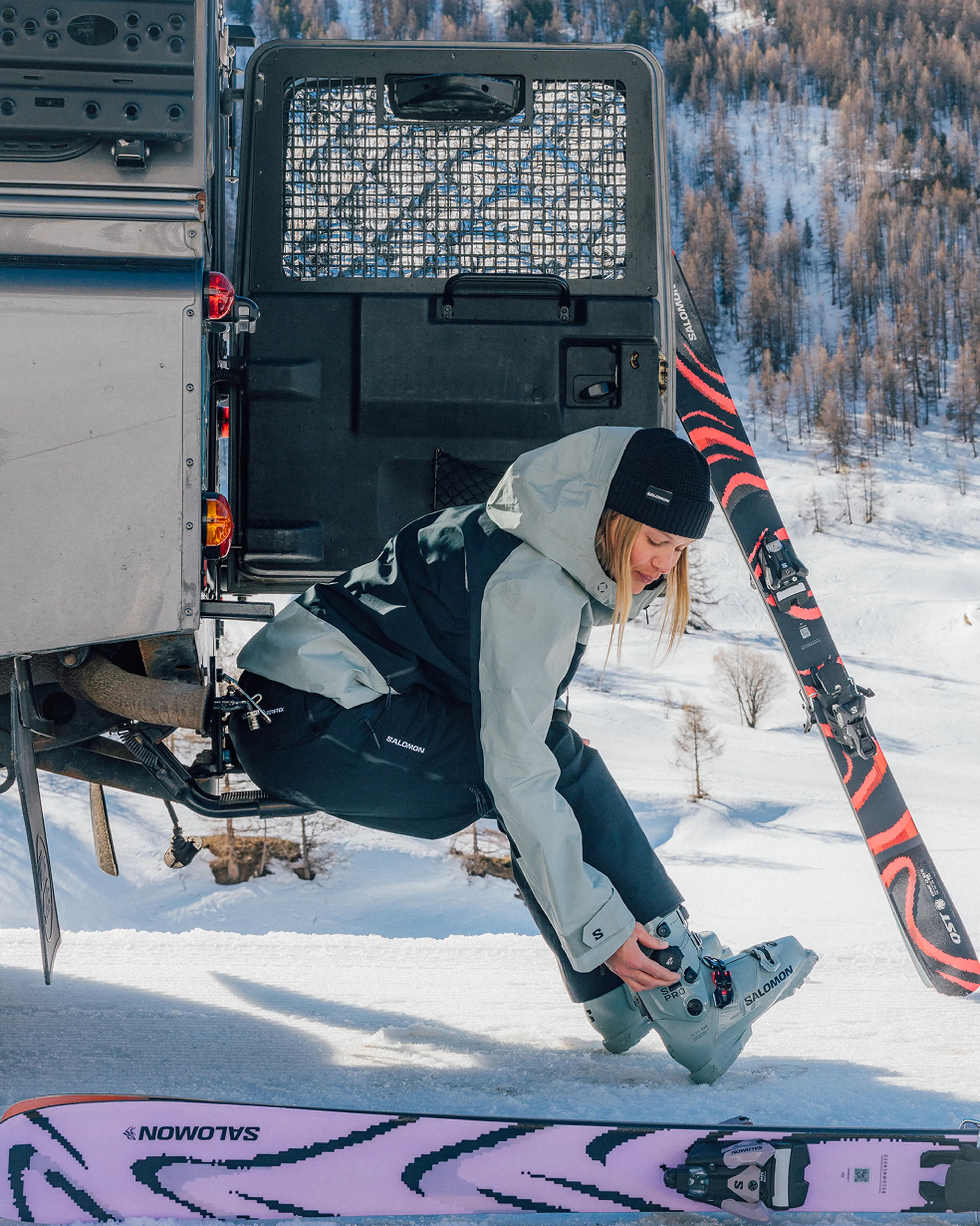 A women sitting in back of car trunk getting ready to ski