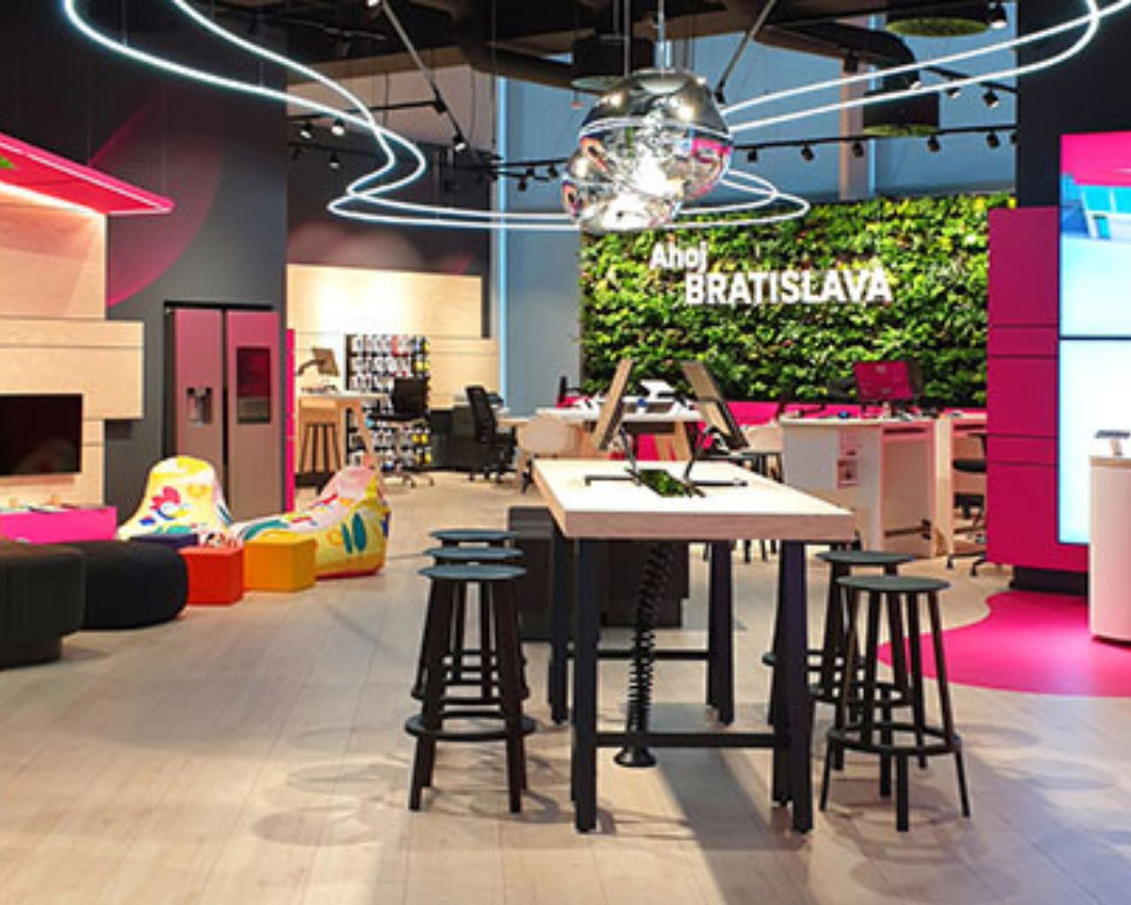 Ako funguje spolupráca s nami Moderný interiér predajne Telekom s centrálnym stolom, stoličkami, neónovými svetlami a zelenou stenou s nápisom „Ahoj Bratislava“. Svetlá a farebná výzdoba.