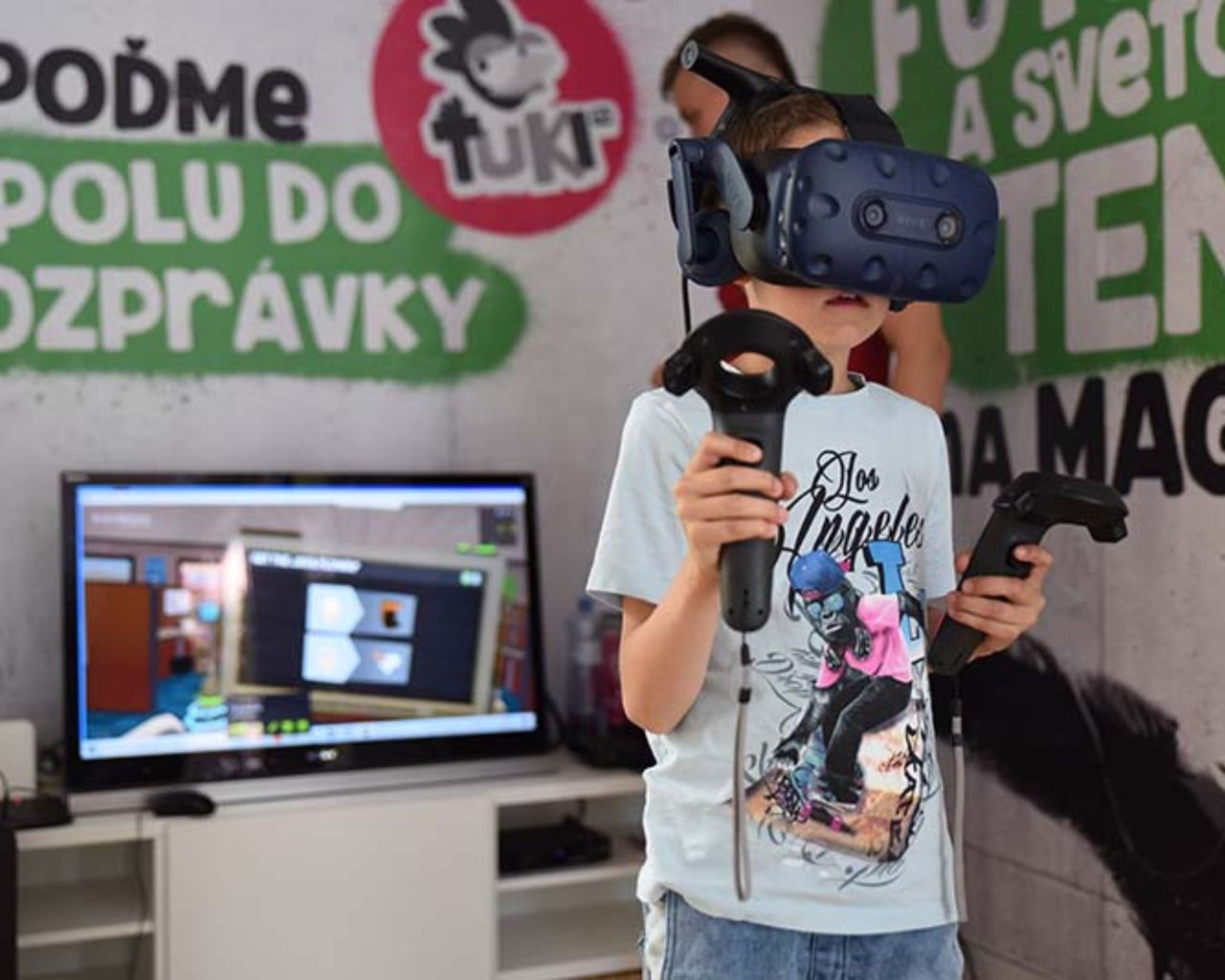 Dieťa s VR headsetom a ovládačmi v ruke hrá hru v miestnosti s farebnou nástennou grafikou a televíznou obrazovkou, na ktorej sa hra zobrazuje.