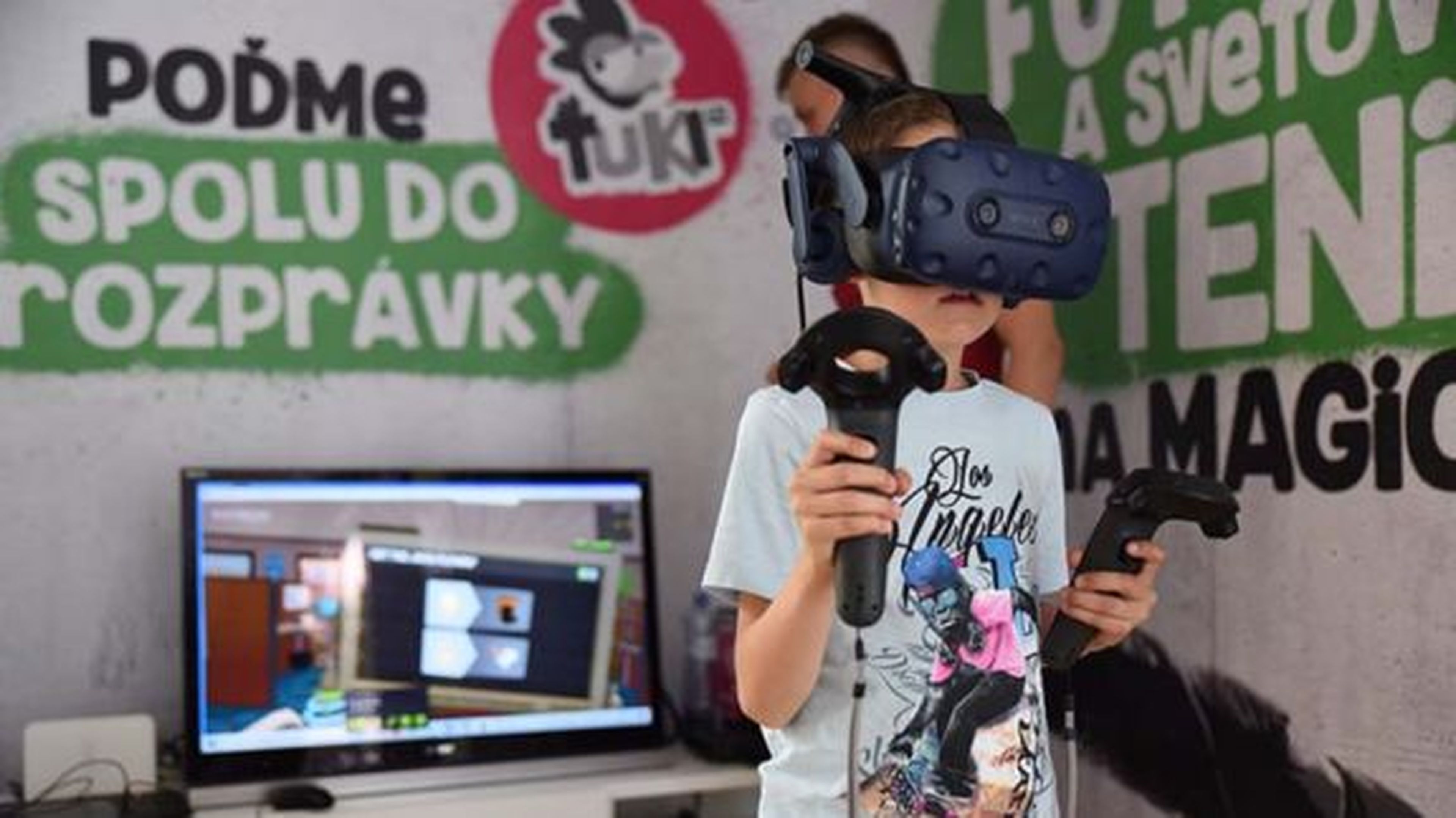 Dieťa s VR headsetom a ovládačmi v ruke hrá hru v miestnosti s farebnou nástennou grafikou a televíznou obrazovkou, na ktorej sa hra zobrazuje.