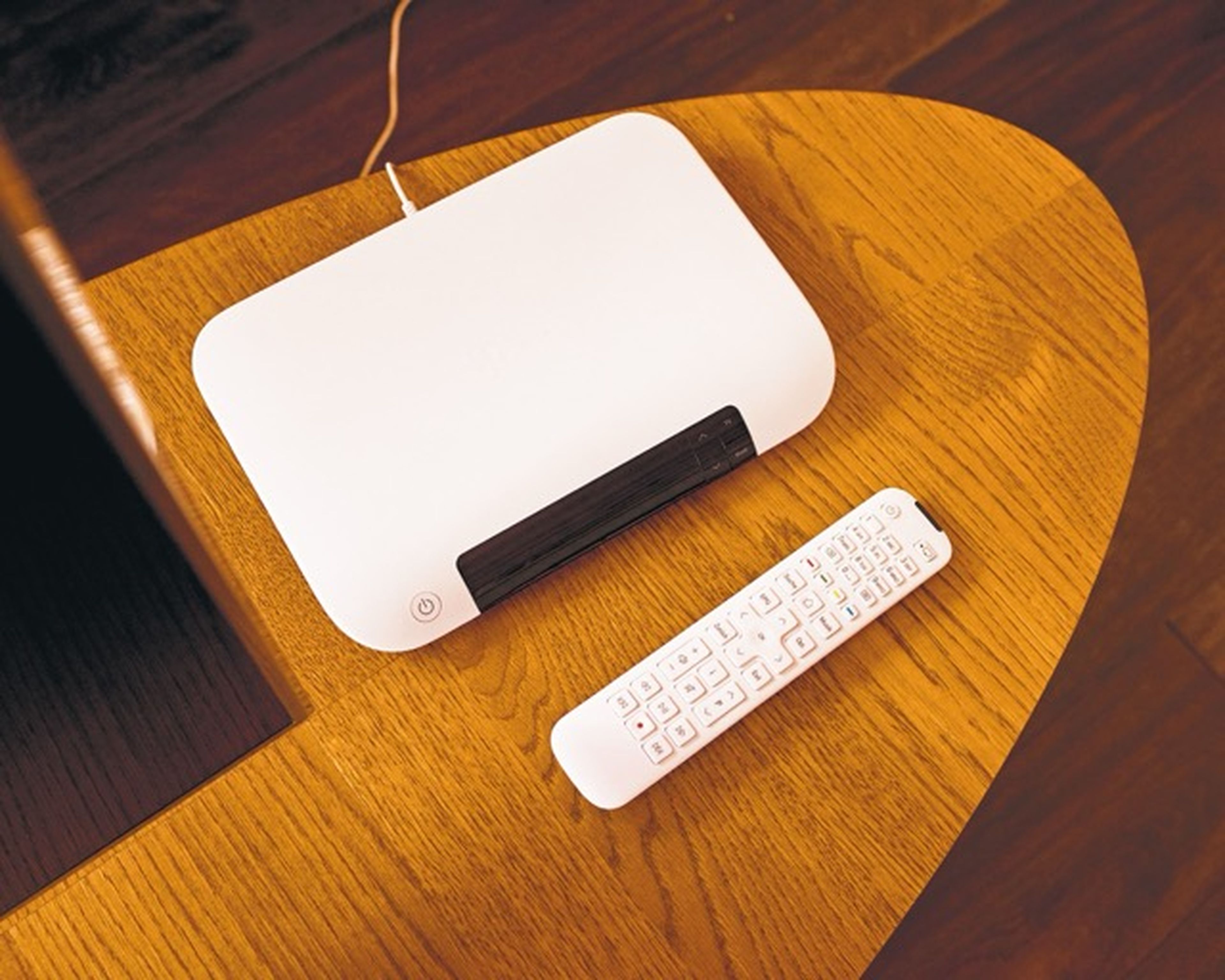 Biely modem a zodpovedajúce diaľkové ovládanie na drevenom oválnom stole.