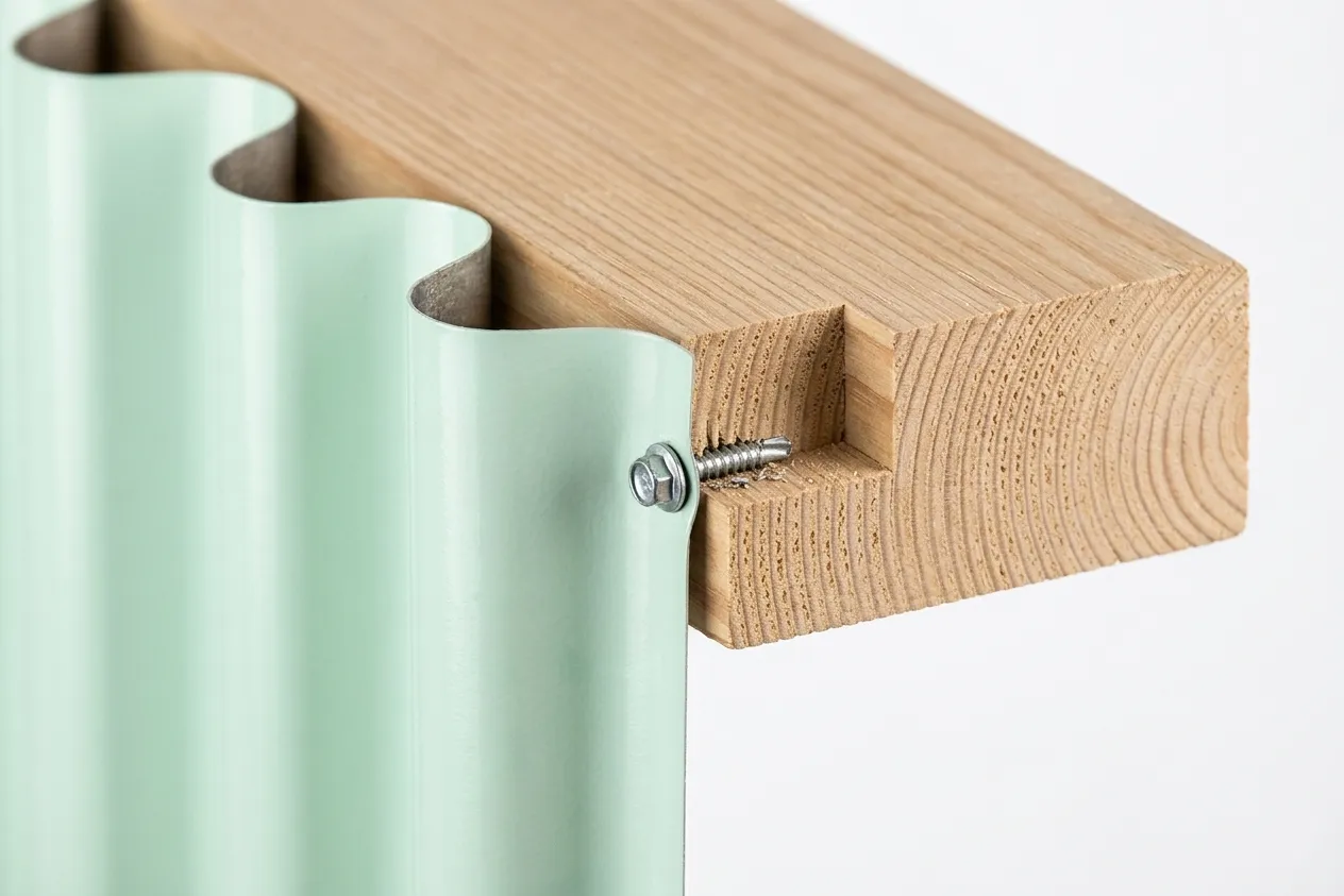 Close-up of a wavy mint green panel attached to a wooden piece with a screw, showing grooves in the wood.