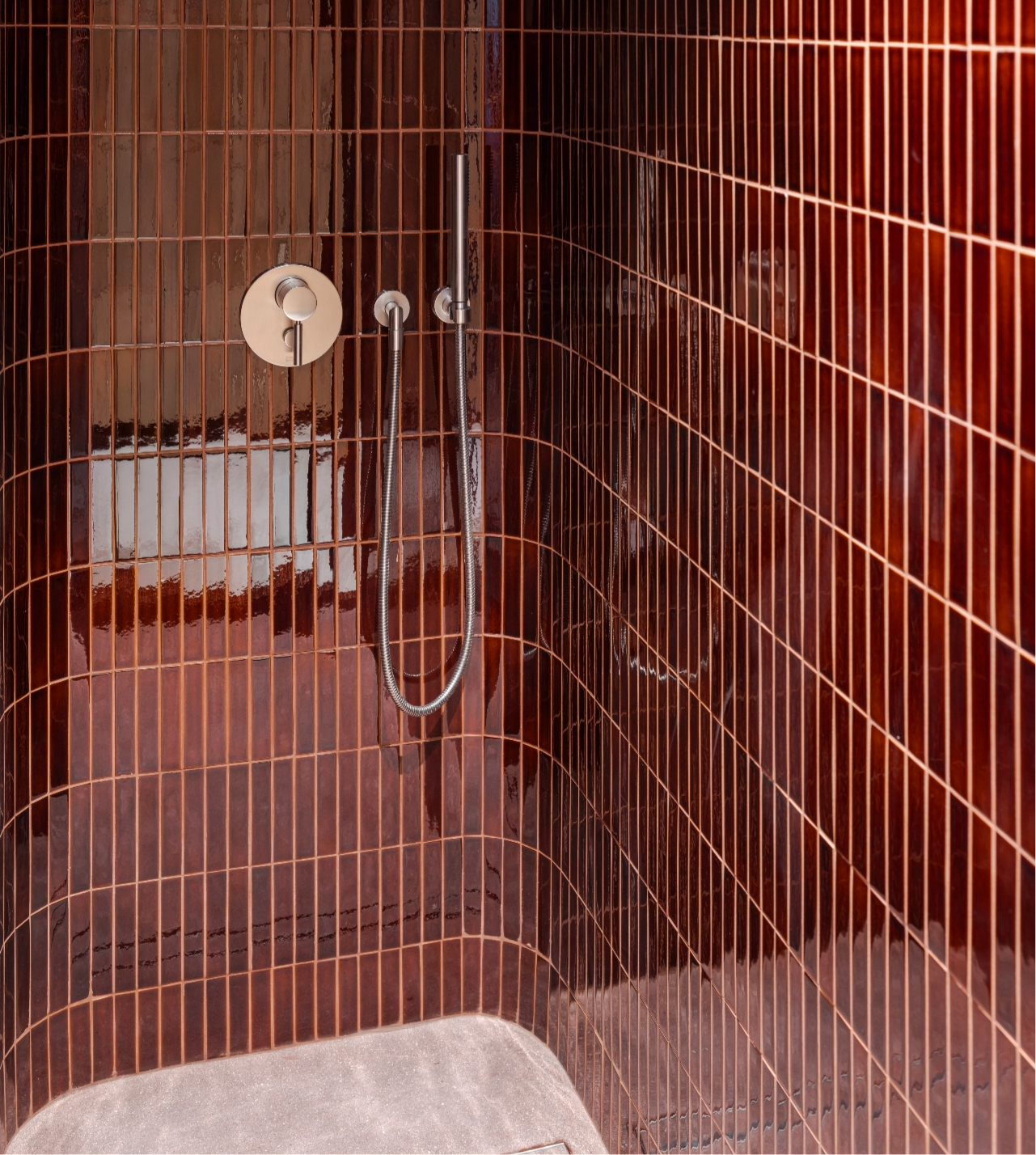 260121-1148-F5935-RT-FINAL-5K@2x Shower area with curved brown tile walls, a minimalist round faucet, and a sleek hand-held showerhead.
