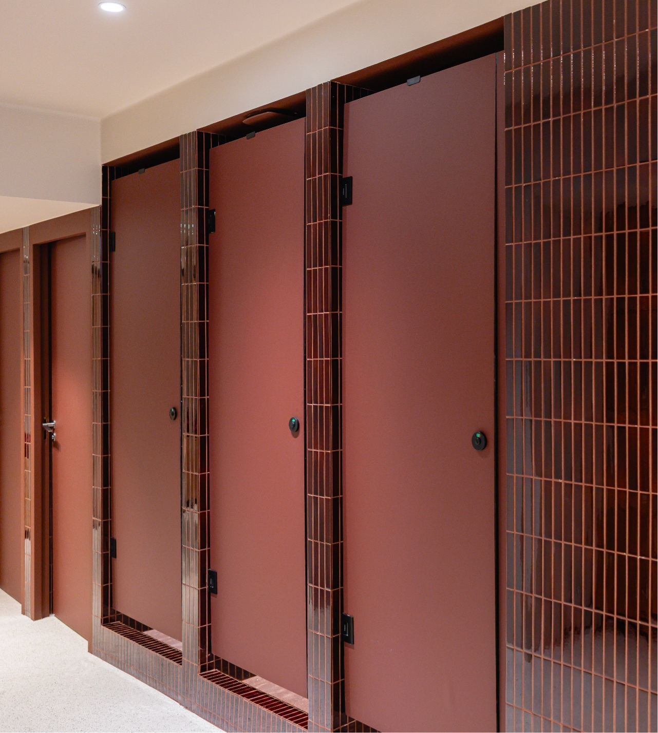 0070_20260121_MOREL__MG_4217_HD_Caudalie@2x A row of red restroom stalls with matching doors and brick-patterned tiles, creating a clean and modern look.