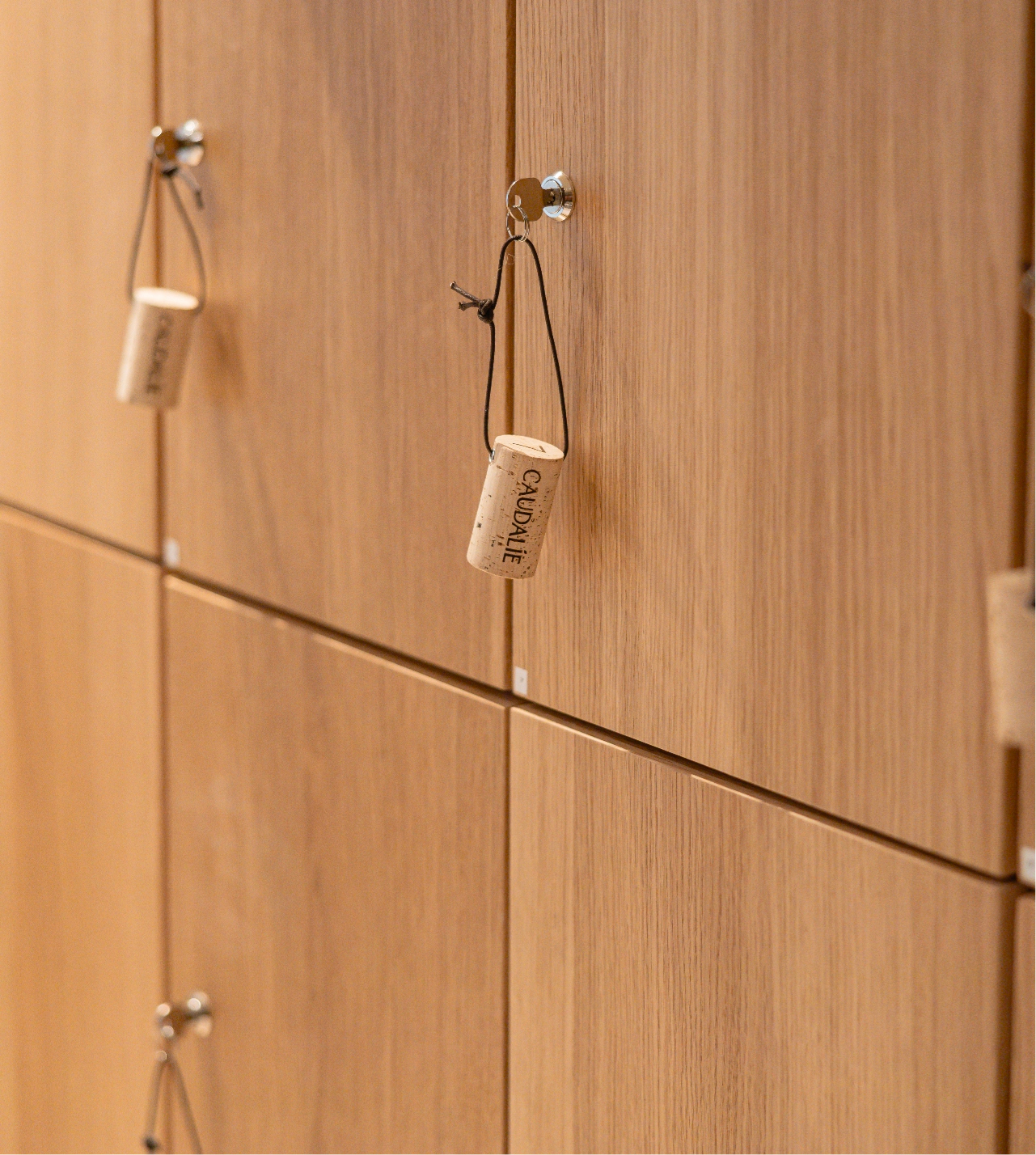 0073_20260121_MOREL__MG_4233_HD_Caudalie@2x Wooden lockers with cork handles on a wall, each featuring a labeled string for easy opening.