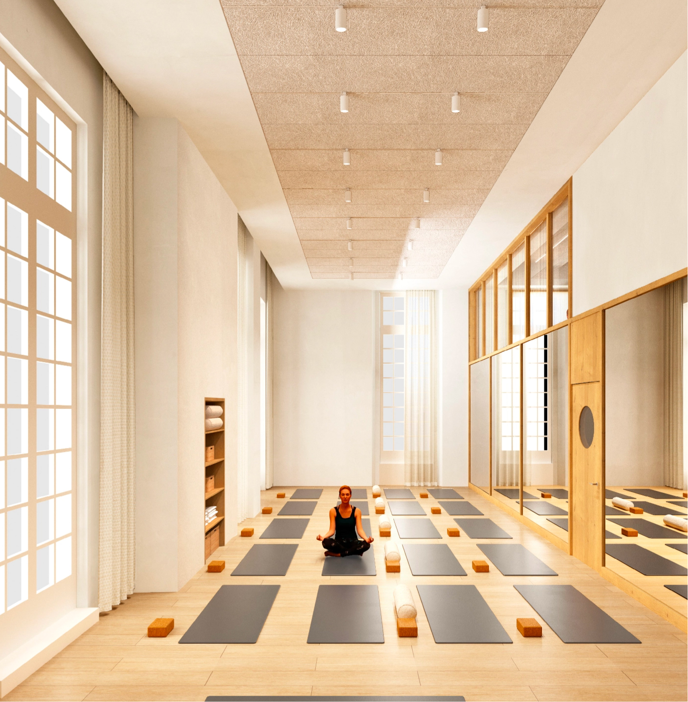 Caudalie Studio A tranquil yoga studio with large windows, wooden floors, yoga mats, and blocks arranged neatly. A person sits cross-legged in the center.