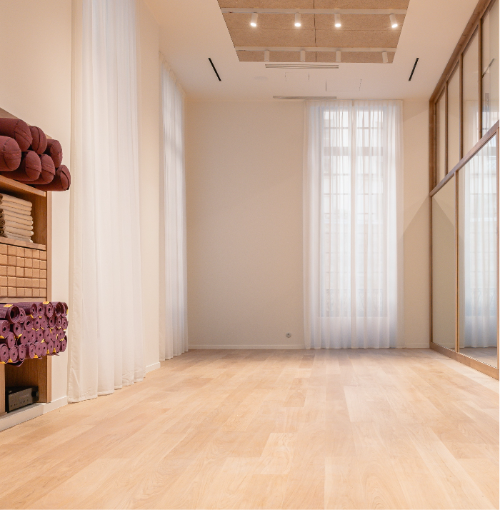 0067_20260121_MOREL__MG_4197_HD_Caudalie Bright, empty yoga studio with wooden floors, stacked mats and towels, large mirrors, and sheer curtains filtering natural light.