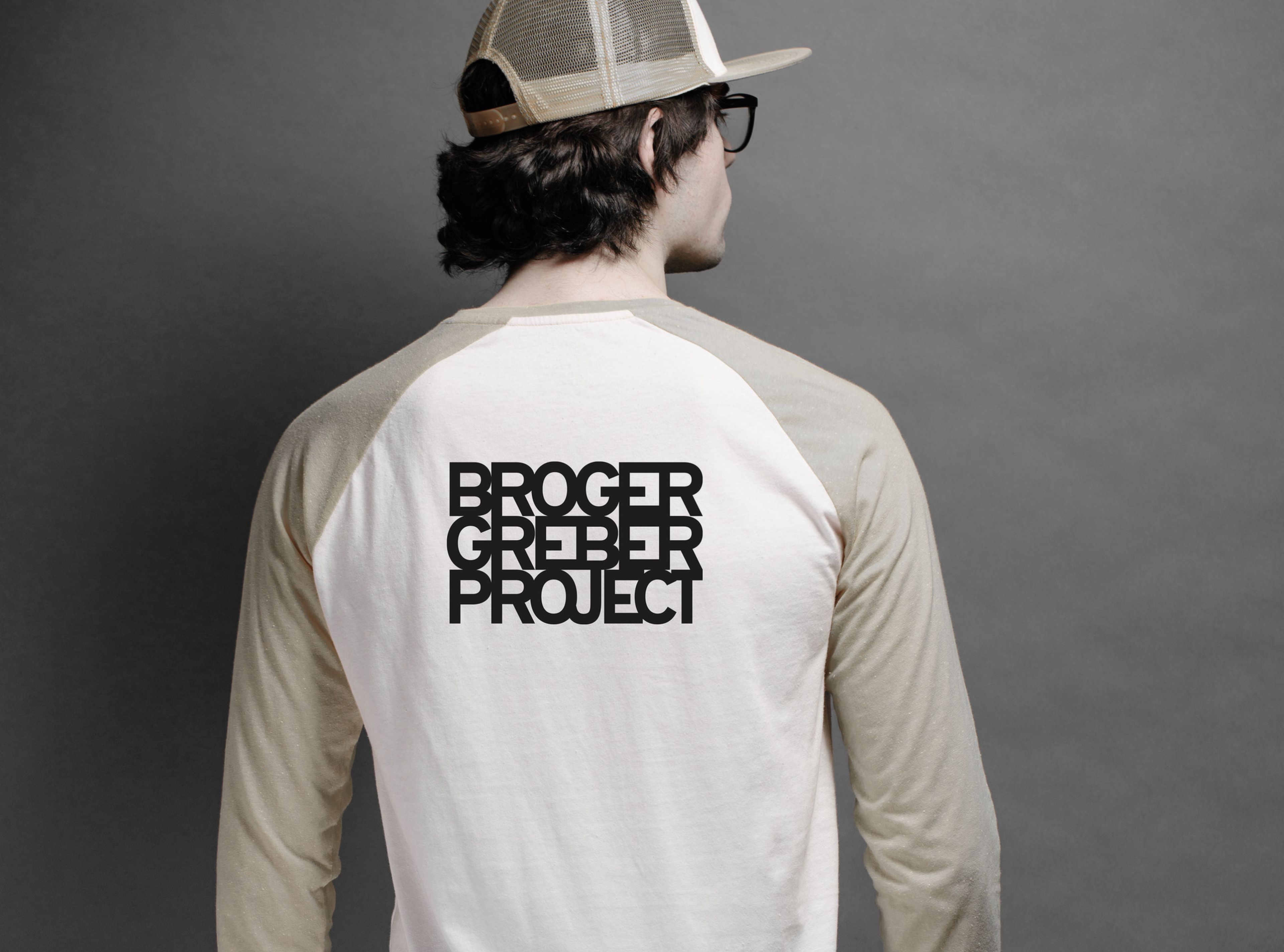 Person, die ein beige-weißes Langarmhemd mit dem Schriftzug „BROGER GREBER PROJECT“ auf der Rückseite und eine beige Kappe trägt.