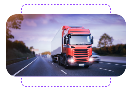 Red semi-truck driving on a highway with blurred trees and sky in the background, lights on and motion blur.