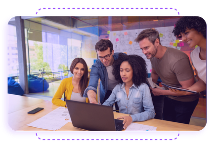 A group of five people gathered around a laptop in a bright office, collaborating on a project with drawings and sticky notes in the background.