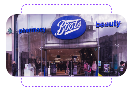 Entrance of a Boots store with large glass doors, displaying "pharmacy" and "beauty" signs, and people entering and exiting.