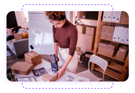 A person scanning a package in an office setting, surrounded by boxes and paperwork on a desk.