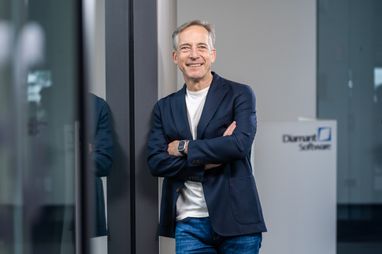 Sven Krüger lehnt lächelnd an einer Wand. Im Hintergrund das Logo Diamant Software.