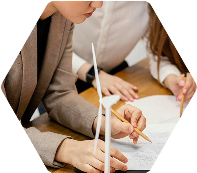 Two people working on wind turbine designs, using pencils on paper. A small wind turbine model is on the table.
