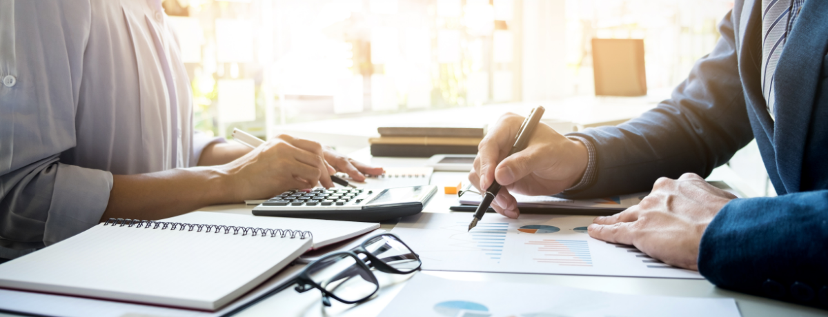Close-up of two professionals reviewing financial charts and using a calculator at a desk with notebooks and glasses, representing BMWL’s comprehensive accounting and assurance service offerings.