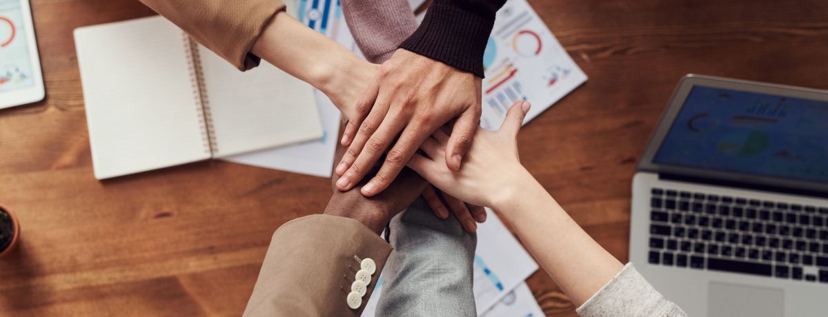 Diverse group of hands joined together over a wooden table with documents and a laptop, symbolizing nonprofit associations supported by BMWL’s accounting and assurance services.