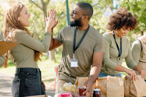 Volunteers high-fiving while organizing food donations at an outdoor charity event, illustrating activities commonly associated with charitable organizations served by BMWL’s accounting and assurance services.