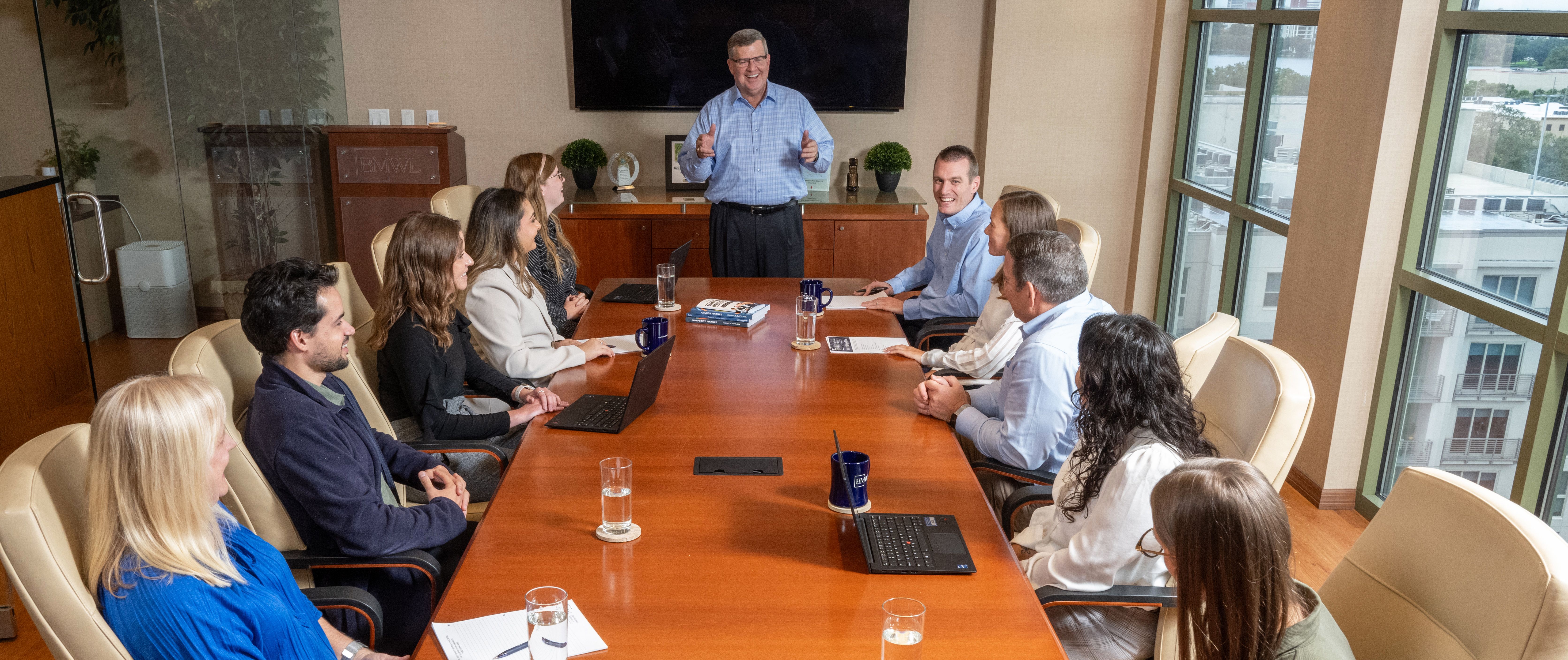 BMWL team members seated in a conference room around a table, listening to a managing partner, Mike Batts, standing and speaking at the front