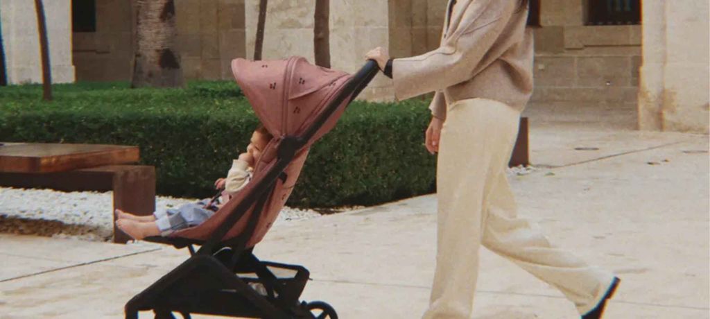 Person pushing a baby in a pink stroller through an outdoor area with stone paths and greenery.