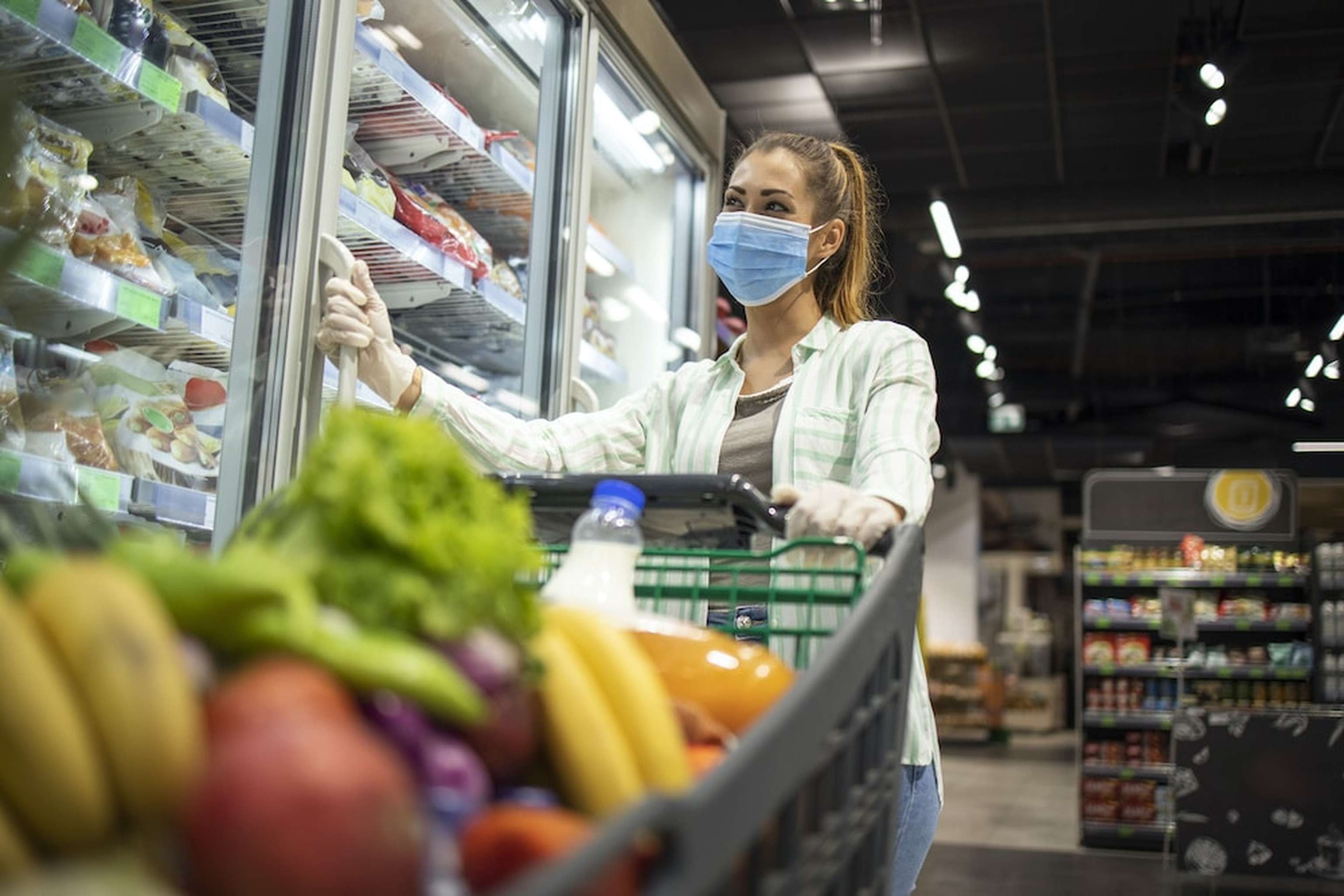 Woman With Protective Mask And Gloves Shopping In Supermarket During COVID 19 Pandemic Or Corona Virus. Protect Yourself Against Highly Contagious Coronavirus.