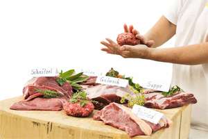Verschiedene Fleischsorten mit Namensschildern auf einem Tisch. Hände formen Hackfleisch.