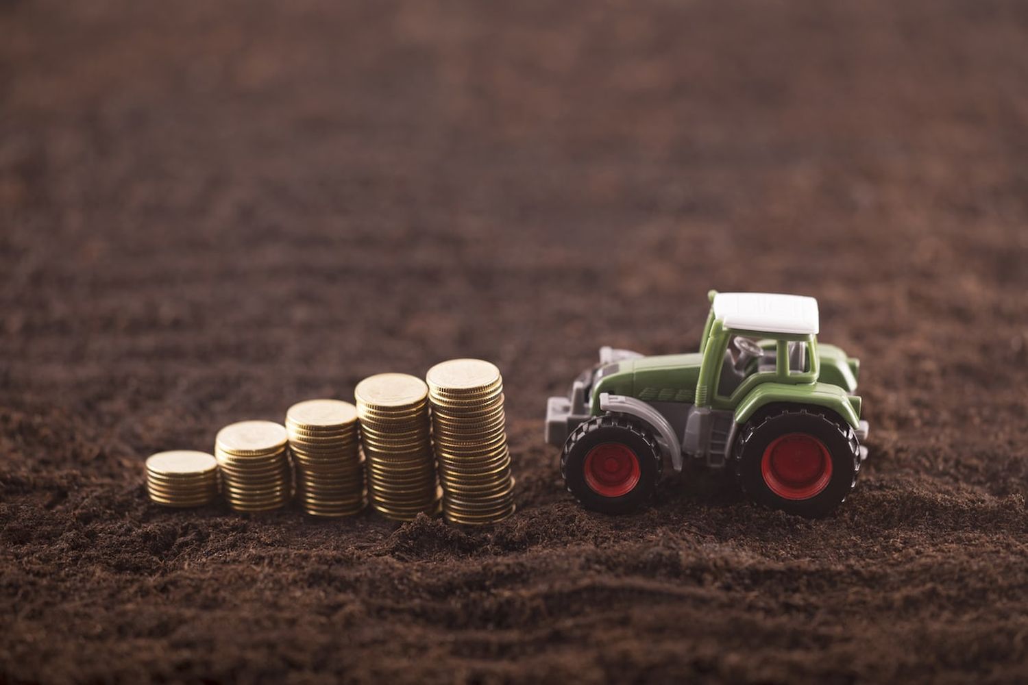 Tractor Miniature With Coins On Fertile Soil Land