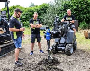 Drei Männer beobachten einen Bohrer an einem Raupenfahrzeug, das in einem grünen, bewaldeten Gebiet arbeitet.