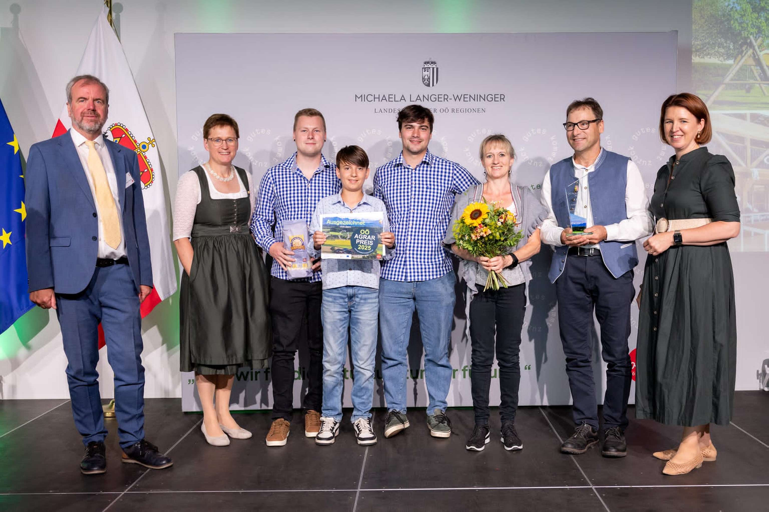 Gewinner des Dritten Platzes der Kategorie Einkommen stehen mit dem Preis und politischen Vertretern auf der Bühne.