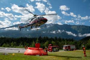 Österreichischer Polizeihubschrauber befüllt Löschwasserbehälter der Feuerwehr Tirol bei Übung in alpiner Landschaft.