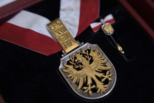 Österreichische Medaille mit Goldadler auf schwarzem Hintergrund und rotem Band; daneben eine Miniaturversion.