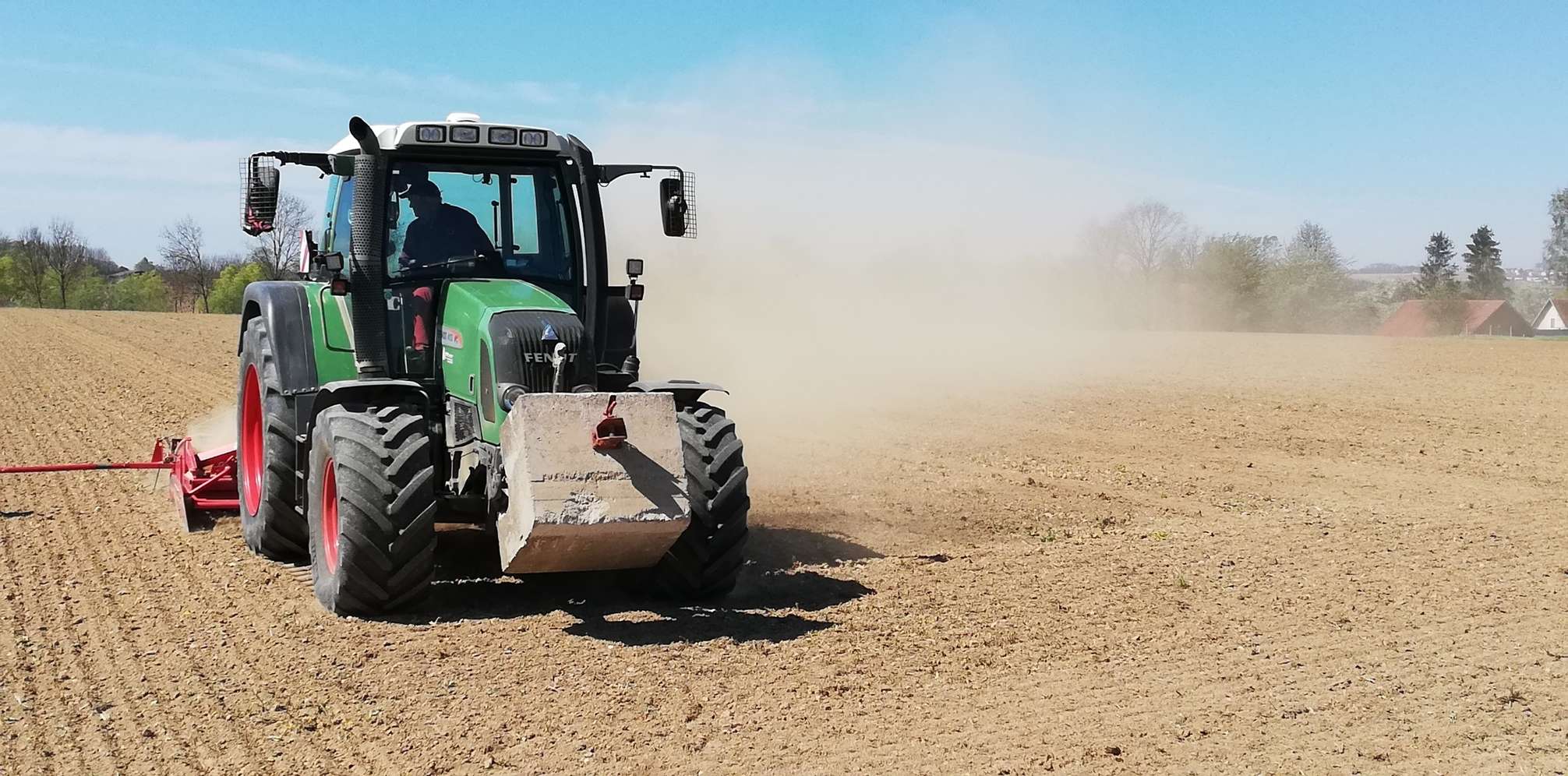 Traktor auf dem Feld wirbelt Staub auf.