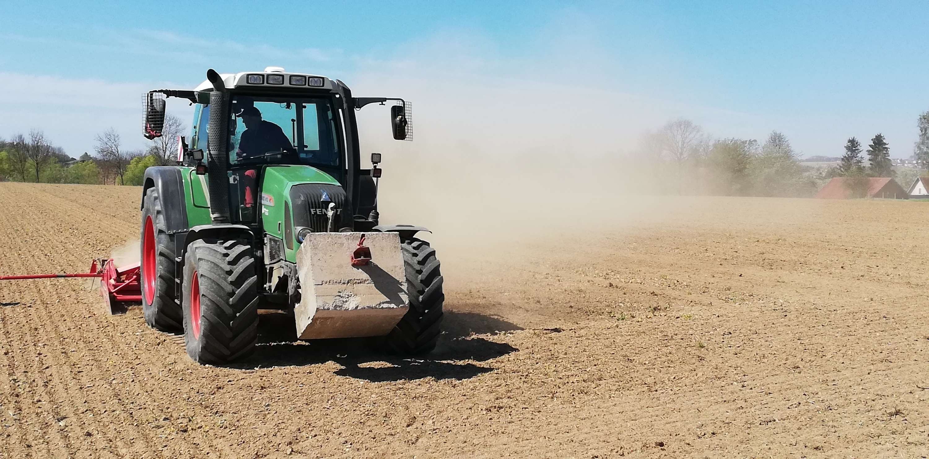 Traktor auf dem Feld wirbelt Staub auf.