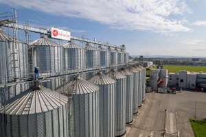 Aerial view of large metal silos at an agricultural facility with "Vfi Oils for Life" sign, under a partly cloudy sky.