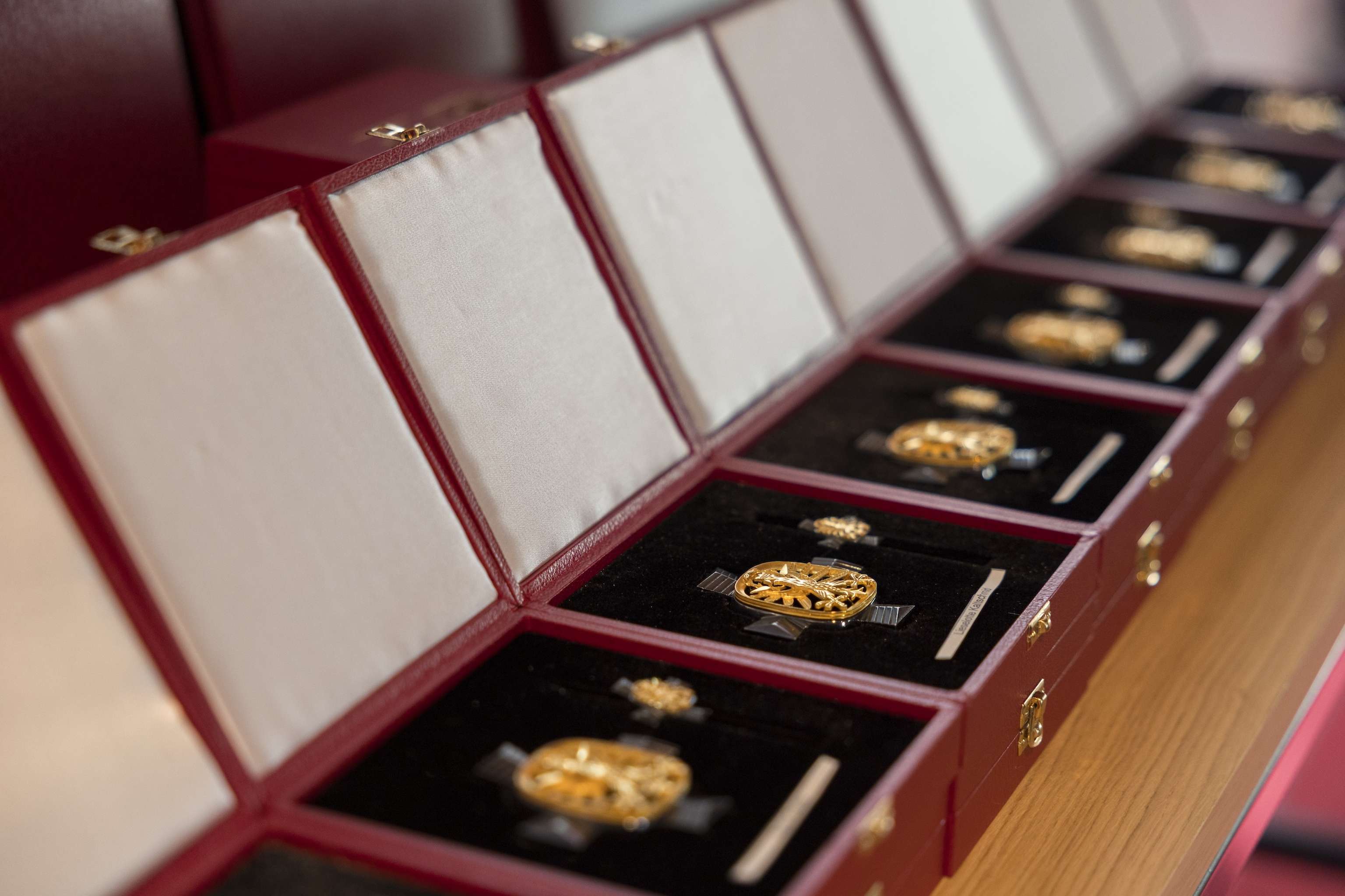 Open red boxes with gold medals displayed in a row on a wooden surface.