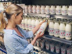 Eine Frau nimmt eine Flasche Milch mit Tierhaltung-plus-Siegel aus dem Supermarktregal.