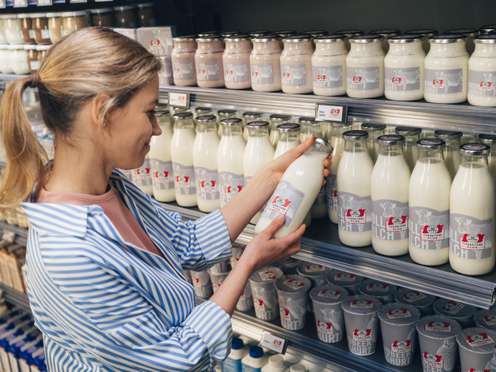 Eine Frau nimmt eine Flasche Milch mit Tierhaltung-plus-Siegel aus dem Supermarktregal.