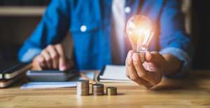 Business Woman Hand Holding Lightbulb With Using A Calculator To