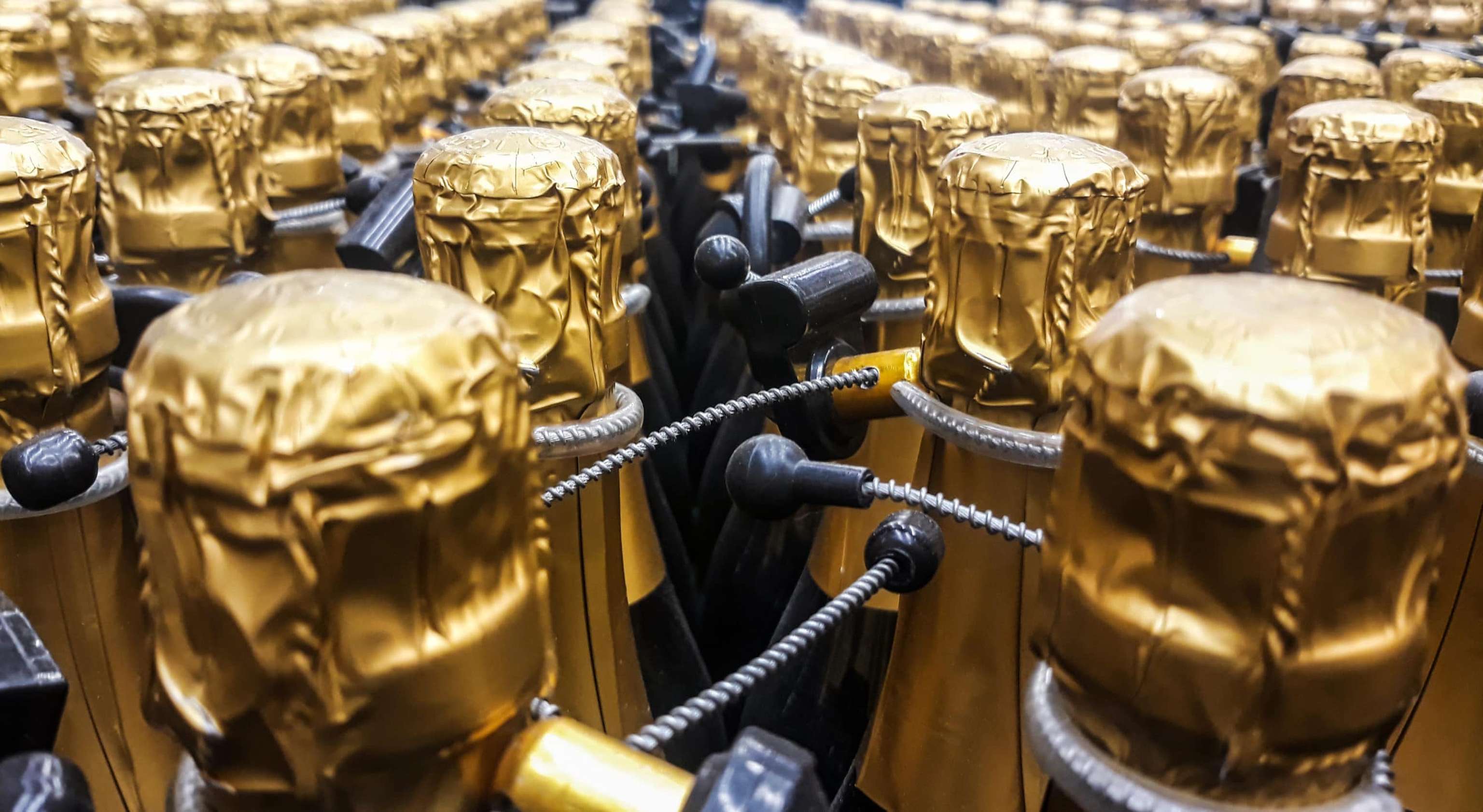 Many Bottles Of Champagne With Gold Foiled Bottleneck And Anti Theft Systems In Store. Front View