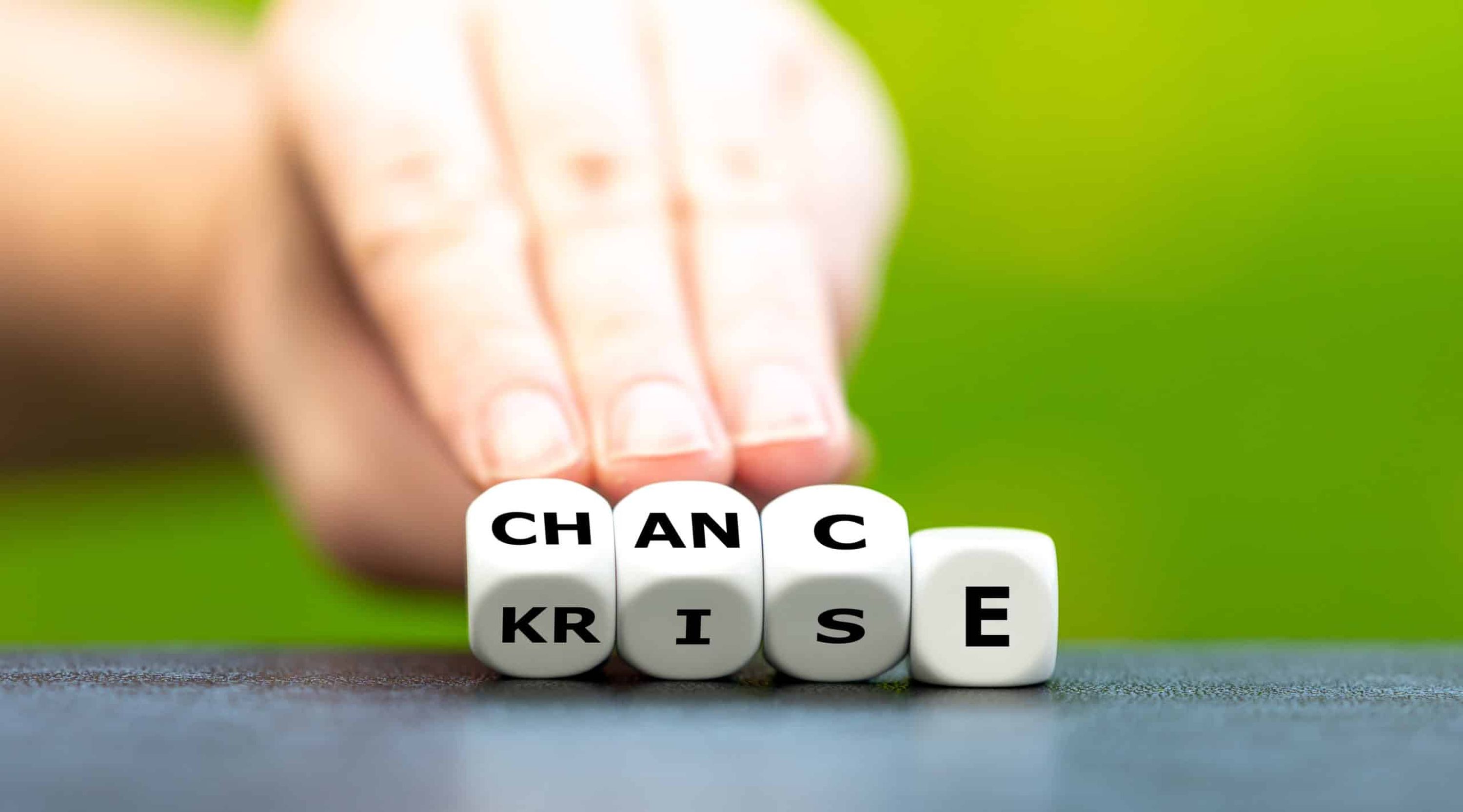 Hand turns dice and changes the German word &#8220;Krise&#8221; (crisis) to &#8220;Chance&#8221; (chance).