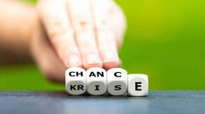 Hand turns dice and changes the German word “Krise” (crisis) to “Chance” (chance).
